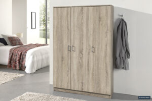 De Opbergkast 'Ray' met 3 deuren en 4 planken in Sonoma staat tegen een witte muur. Een grijze badjas hangt aan een haak vlakbij, terwijl een bed met een rood geruite deken op de achtergrond verschijnt.