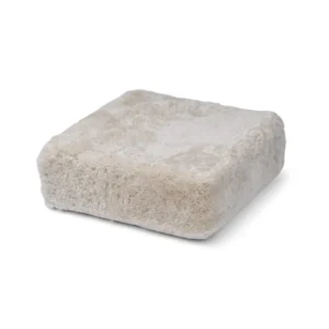 De Poef Schapenvacht Krullend Korte Wol M02 is een vierkant, beige, pluche kussen met een zachte, donzige textuur tegen een witte achtergrond.