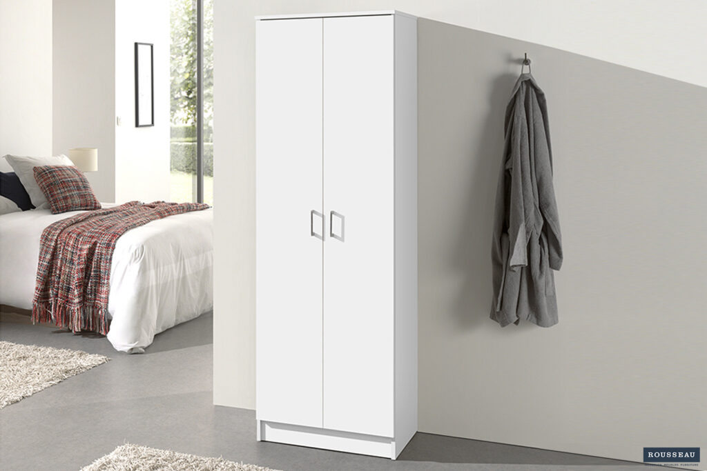 De Opbergkast 'Ray' met 2 deuren en 4 legplanken in wit staat tegen de muur in een moderne slaapkamer. Naast de kast hangt een grijze badjas aan een haak. Op de achtergrond zie je een bed met geruit dekbed.