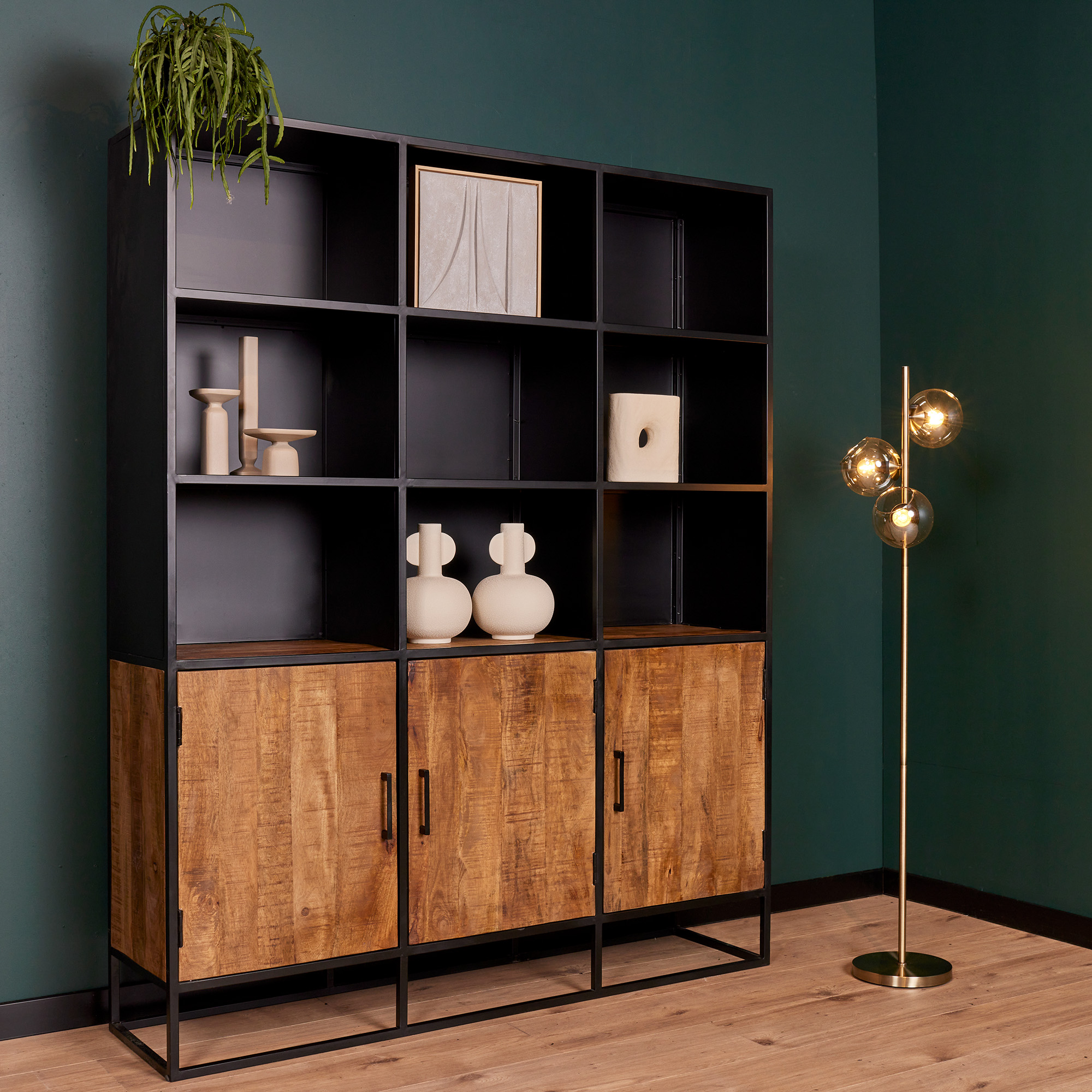 De Boekenkast Oakland XXL | 160 cm, een moderne zwarte stellingkast met houten kasten, is gestyled met minimalistische vazen en abstracte kunst tegen een donkergroene muur. Een gouden vloerlamp met drie bollen staat vlakbij op een lichte houten vloer.