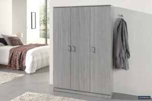 Een moderne slaapkamer is voorzien van de Opbergkast 'Ray' 3 deuren en 4 legplanken Grijze eik kledingkast, een grijs gewaad aan de muur, een bed met wit beddengoed en geruite deken, en een raam dat natuurlijk licht binnenlaat.