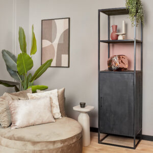Een moderne woonruimte met een ronde beige stoel, kussens met structuur, een Boekenkast Denver Black mangohout en stalen kast met 1 deur en decoratieve vazen, een abstract wandkunstwerk, een groene potplant en een klein bijzettafeltje met een kopje.