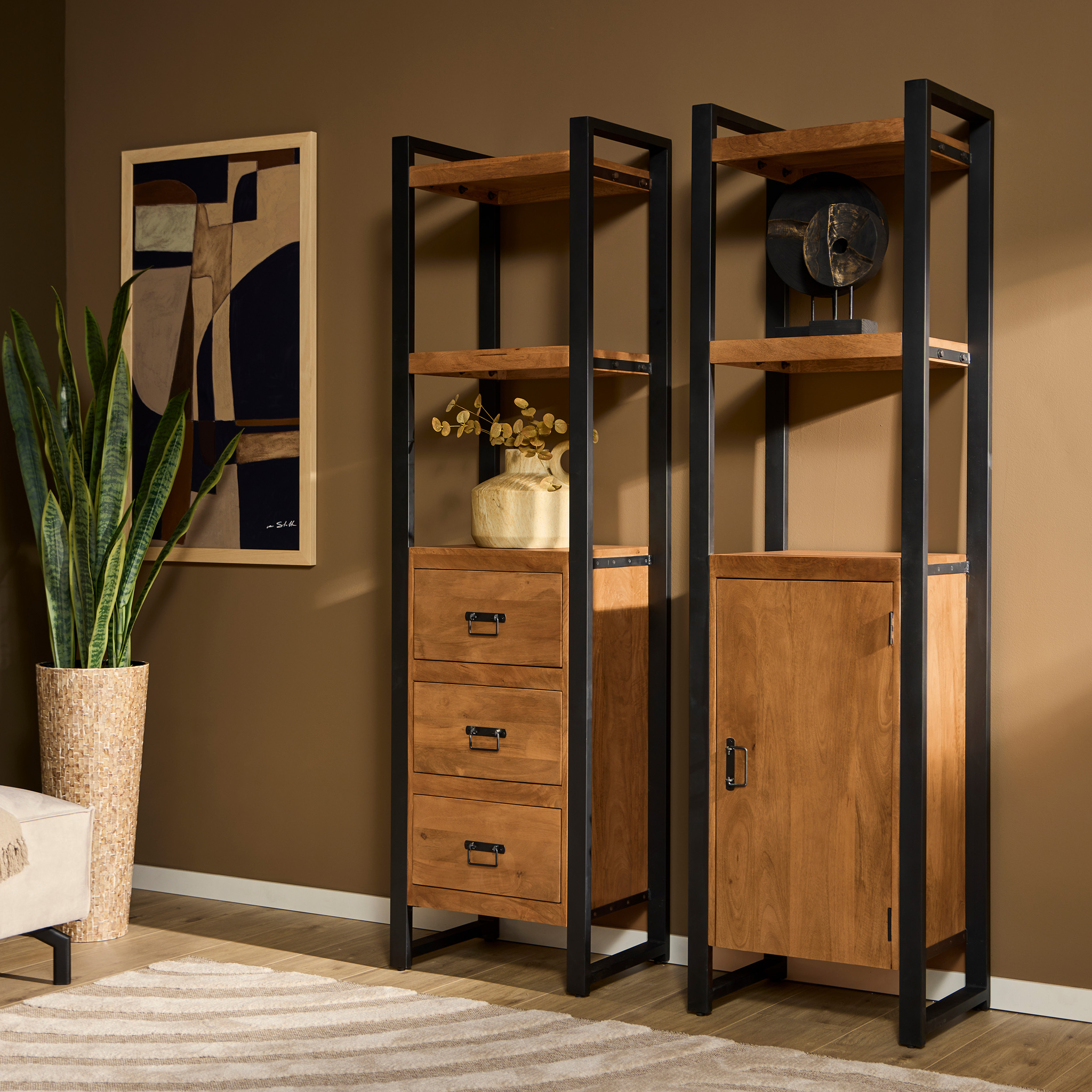 Een moderne woonkamer met de Boekenkast Boaz | 1 deur - een hoge plank met een kast - gecombineerd met metalen accenten, een plant, abstracte muurkunst en een beige vloerkleed voor een stijlvolle afwerking.