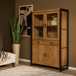 Een moderne woonkamerhoek met de Vitrinekast Boaz 115 cm, een hoge houten kast met glazen deuren, in combinatie met een slangenplant, abstracte muurkunst, een beige bank en plaid, plus een rond beige vloerkleed op een houten vloer.