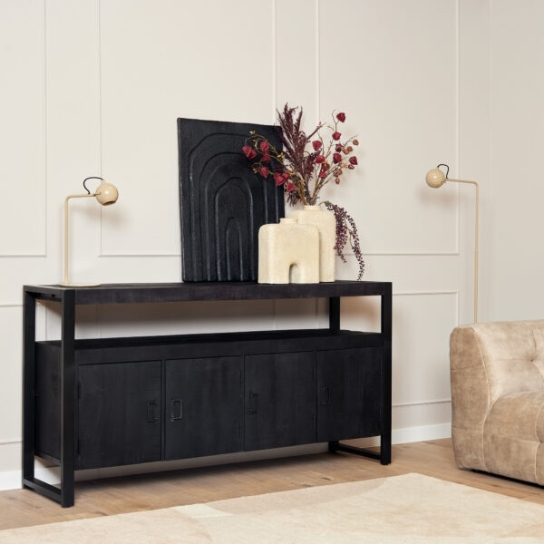In een moderne woonkamer staat de Dressoir Boaz Black 175 cm, versierd met een minimalistisch decor, abstracte sculpturen, een vaas met gedroogde bloemen en twee globe vloerlampen. Een beige sofa staat rechts tegen een wand met panelen.