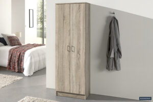 Een moderne slaapkamer met de Opbergkast 'Ray' 2 deuren en 4 legplanken Sonoma (1c) kledingkast, een bed met een geruit deken en een grijze badjas aan een wandhaak. Zonlicht uit het raam versterkt de minimalistische sfeer.