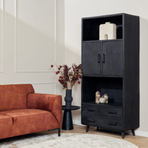 Een moderne woonkamer heeft een roestkleurige bank, een zwarte bijzettafel met een vaas van gedroogde bladeren, de Boekenkast Omaha Black | 90 cm met decoratieve items en een licht rond vloerkleed op een lichte houten vloer.