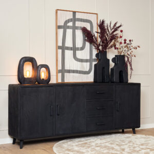 De Dressoir Omaha Black 220 cm staat tegen een neutrale muur, met daarop twee abstracte lampen, twee vazen met droogbloemen en een opgestoken kunstwerk van zwarte lijnen. Op de vloer ervoor ligt een rond beige vloerkleed.