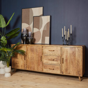 De Dressoir Omaha 220 cm, met drie lades en twee kastjes, staat tegen een donkerblauwe muur, versierd met geometrische kunst, vazen, een zwarte kandelaar en potplanten op een lichthouten vloer.