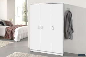 De Opbergkast 'Ray' 3-deuren en 4 legplanken in wit staat in een moderne slaapkamer naast een muur met een grijze jas aan een haak. Op de achtergrond zie je een bed met plaid dekentje en een raam.