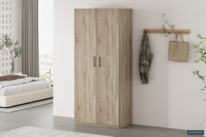De Opbergkast 'Mike' 80 cm 2 deuren Sonoma (2c) staat tegen een witte muur in een moderne slaapkamer, met in de buurt een wandrek met een geruit overhemd en een beige tas. Op de achtergrond zijn een bed en een raam met uitzicht op de stad zichtbaar.