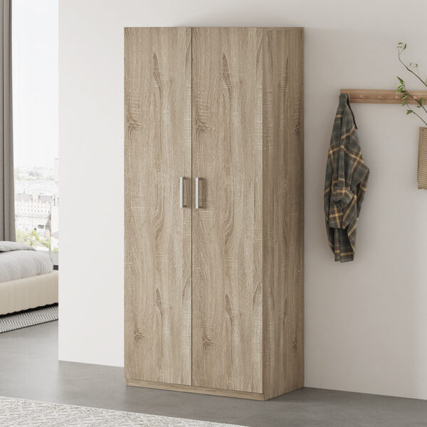 De Opbergkast 'Mike' 80 cm 2 deuren Sonoma (2c) staat tegen een witte muur in een moderne slaapkamer, met in de buurt een wandrek met een geruit overhemd en een beige tas. Op de achtergrond zijn een bed en een raam met uitzicht op de stad zichtbaar.