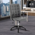 De Bureaustoel 'Luka' Grijs PU (1c), met een modern getuft kussenontwerp, zit voor een bureau met een computermonitor in een hoog kantoor met grote ramen en uitzicht op de skyline van de stad.