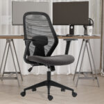 De Bureaustoel 'Claude' Mesh Zwart/Grijs (1c), een moderne ergonomische stoel met netrugleuning en verstelbare hoofdsteun, staat voor een houten bureau met twee monitoren, toetsenbord, muis en beker in een thuiskantoor met beige gordijnen en houten vloeren.