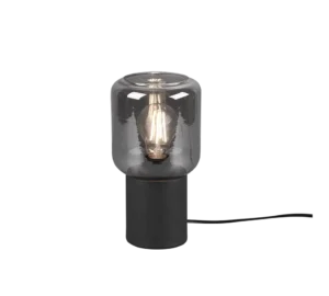 De REALITY Tafellamp NICO heeft een modern ontwerp met een cilindrische zwarte voet en een heldere glazen kap die de gloeiende gloeilamp binnenin onthult.