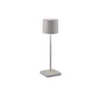 De Reality Tafellamp Fernandez heeft een modern minimalistisch ontwerp met een cilindrische grijze kap, slanke verticale steel en rechthoekige witte voet. Als de lamp aanstaat, werpt hij een zacht, neerwaarts licht - ideaal voor elke moderne ruimte.
