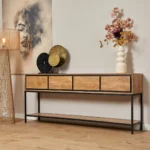 De Sidetable RichWood 180 cm, met vier lades en een zwart metalen frame, staat tegen een beige muur. Bovenop staan decoratieve borden, een witte vaas met bloemen en een staande lamp. Erboven hangt een abstract portretschilderij.