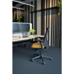 Een modern kantoor met een bureau, twee beeldschermen, een Workliving Nora Mesh Geel Regain ergonomische stoel (NEN1335), een glas water, een notitieblok en een plant in pot, tegen muren met zwart gestreepte panelen en hangend groen.