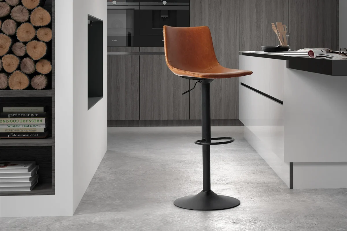 Een moderne keuken met lichtgrijze vloer, houtblokken in een schap, kookboeken op een onderste plank en Barstoel 'Trevi' PU Cognac (2 per doos) met een bruine leren zitting en zwart metalen onderstel op de toonbank.