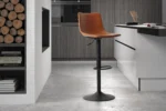 Een moderne keuken met lichtgrijze vloer, houtblokken in een schap, kookboeken op een onderste plank en Barstoel 'Trevi' PU Cognac (2 per doos) met een bruine leren zitting en zwart metalen onderstel op de toonbank.