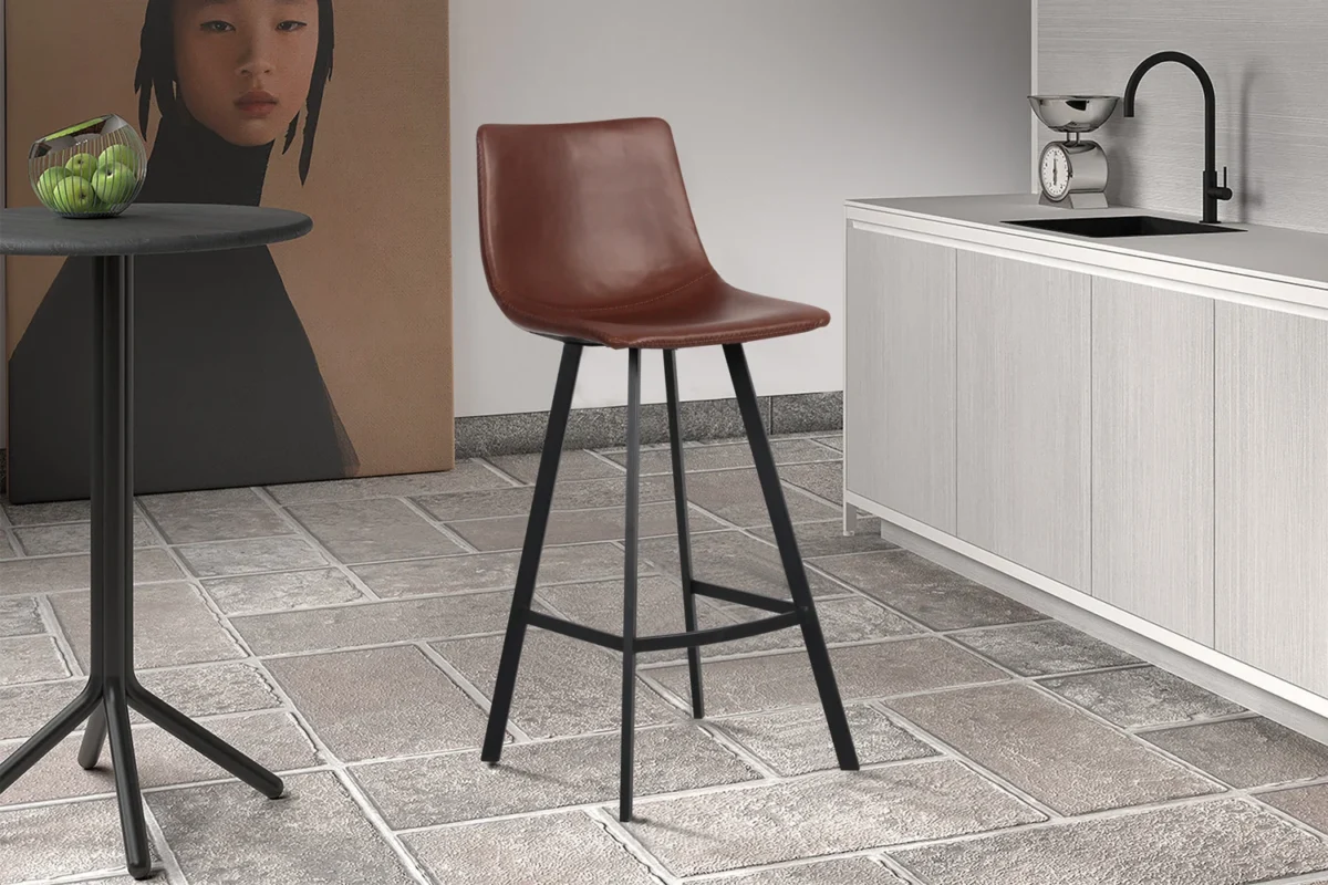 Een moderne keuken toont Barstoel 'Ozan' PU Bruin barkrukken met zwarte metalen poten, een ronde tafel met groene appels, een licht aanrecht met spoelbak en een groot vrouwenportret op de achtergrond.