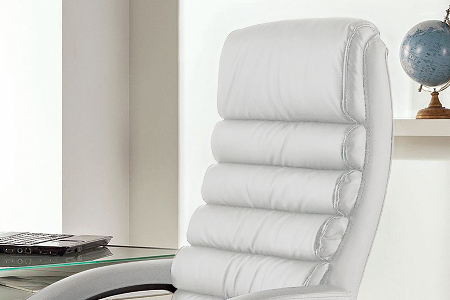 Een modern kantoor met de SALE - Bureaustoel 'Kennedy' PU Wit (1c), een wit gecapitonneerde leren stoel naast een glazen bureau met een gesloten laptop en een blauwe wereldbol op een witte plank op de achtergrond.