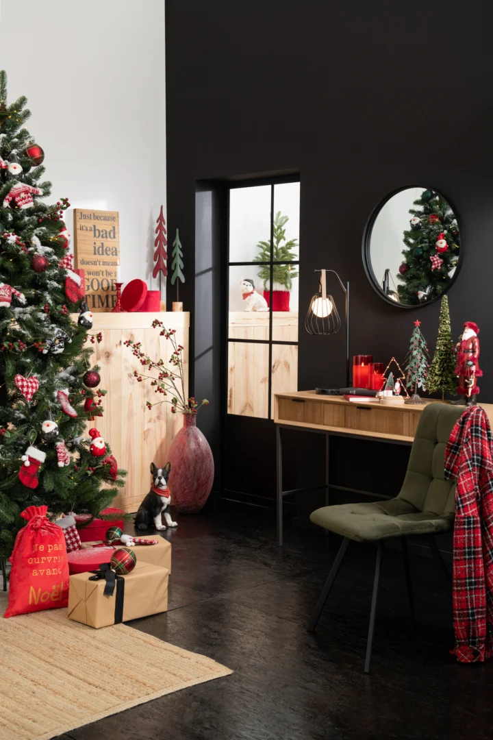 Een gezellige kerstkamer met een versierde boom, ingepakte cadeaus, feestelijke ornamenten, een bureau met de Mirror Round High Border Metal/Glass Black Small en een groene stoel gedrapeerd met een rood geruite deken tegen een zwart-witte muur.