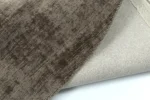 Een close-up van het Vloerkleed Rond Handgemaakt Viskose Grijs tapijt, gevouwen om het grijze oppervlak met textuur en de lichter geweven onderkant tegen een witte achtergrond te laten zien.
