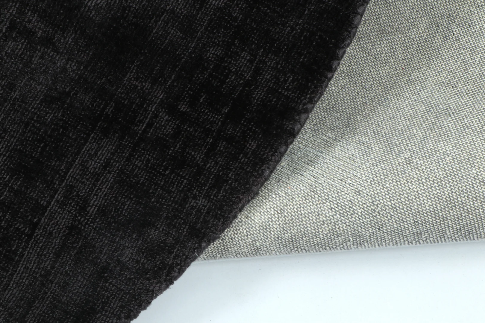 Een close-up van twee overlappende stofstalen: de donkere, zachte en gestructureerde is van Vloerkleed Rond Handgemaakt Viscose Zwart, gedrapeerd over een lichtere, geweven stof op een wit oppervlak.