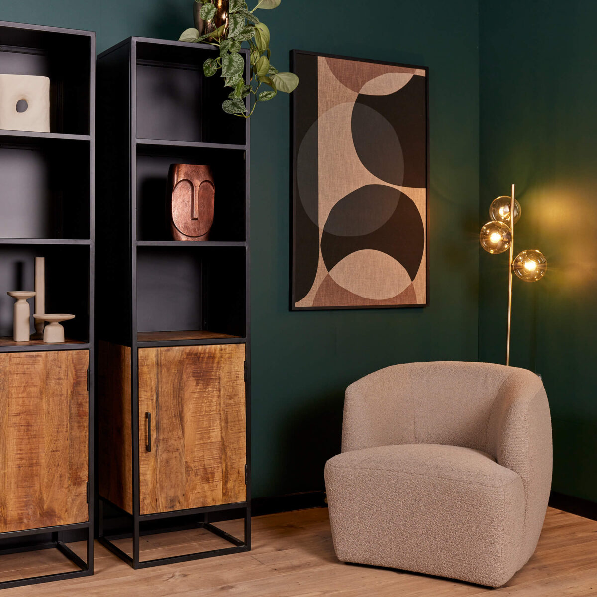 Een moderne woonkamer met donkergroene muren, de Boekenkast Oakland | 50 cm rekken met houtaccenten, abstracte muurkunst, een beige boucle fauteuil en een vloerlamp met drie gloeilampen.