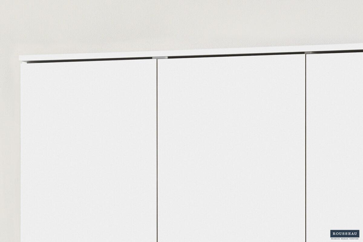 Close-up van het bovenste gedeelte van de Opbergkast 'Ray' 3 deuren en 4 legplanken Wit (2c), een minimalistische witte kast, tegen een lichte muur; een klein Housebad-logo verschijnt in de rechterbenedenhoek.