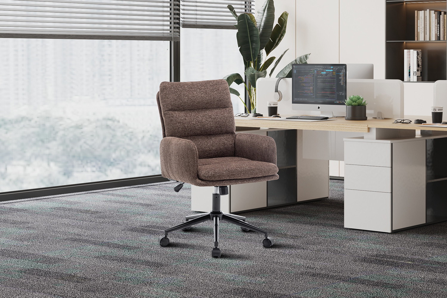 De Bureaustoel 'Aimé' Stof Fabb Raven 45 in bruin staat aan een modern bureau met een computermonitor in een lichte kantoorruimte met grote ramen, vloerbedekking en een plant in pot.