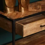 Een close-up van de Sidetable Arlington 2 lades toont het houten blad met chevronpatroon, een zwart metalen frame, een gedeeltelijk geopende lade en twee gouden decoratieve objecten bovenop.