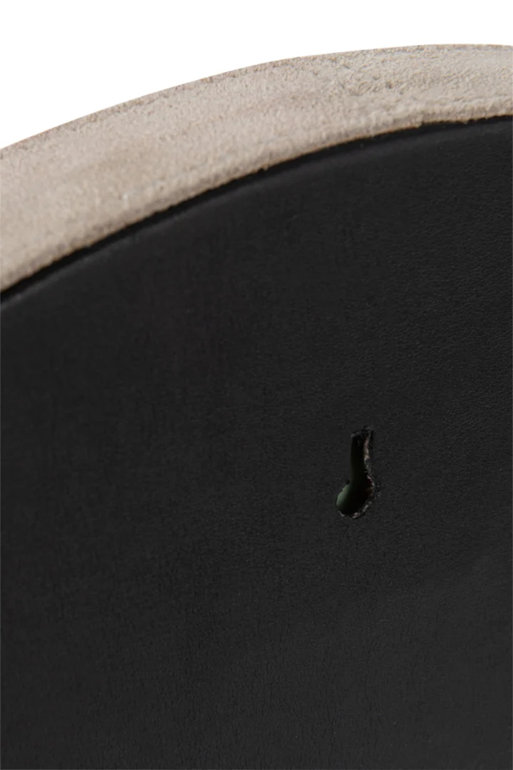 Close-up van Mirror Round Leather Beige Small met een klein druppelvormig gaatje in het midden. Het zwarte leren oppervlak contrasteert met de onafgewerkte, lichtbeige onderkant die zichtbaar is aan de bovenrand.