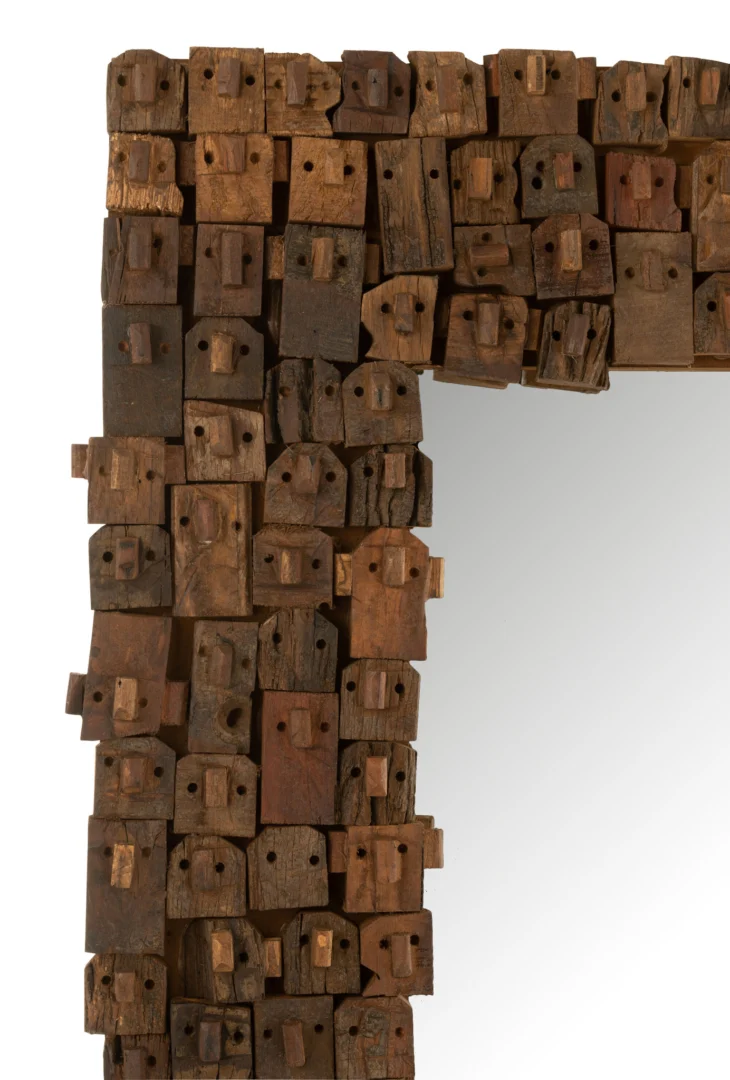 Close-up van het MIRROR SYMA RECYCLED WOOD/MIRROR NATURAL LARGE frame, gemaakt van verweerde houten blokken met gaten en inkepingen, die een gestructureerd, oneffen ontwerp vormen; gedeeltelijke spiegelreflectie rechts.