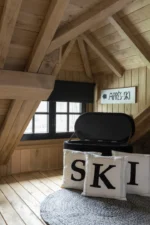 Een gezellige houten zolderkamer met zichtbare balken, een Vloerkleed Miami Outdoor Poly Zwart/Wit Klein, een bank met kussens van SKI en een bord van APRÈS-SKI met een pijl naar links.