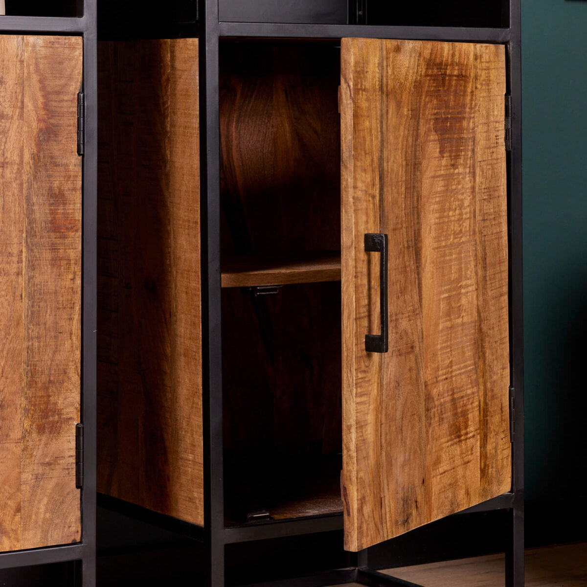 Een close-up van de Boekenkast Oakland | 50 cm toont de houten kast met een zwart metalen frame en een gedeeltelijk open deur die een plank onthult. Het hout heeft een natuurlijke, rustieke afwerking met zichtbare nerfpatronen.