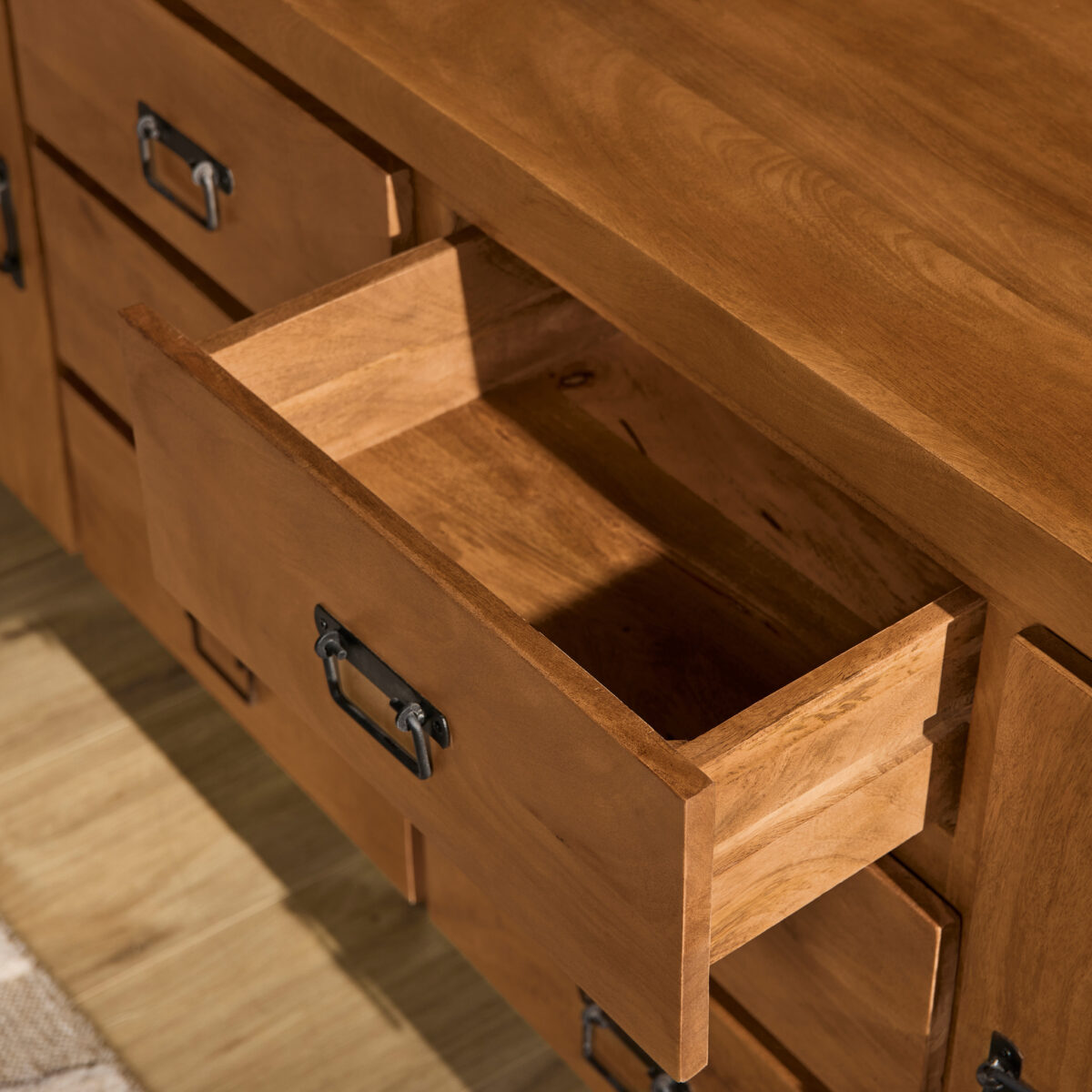 Een close-up van de Dressoir Boaz 200 cm toont een open lade met een lege binnenkant, metalen handgrepen en een lichte houten vloer naast een vloerkleed.