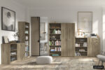 Moderne woonkamer met de SALE - Opbergkast 'Space' 2 deuren en 5 legplanken Sonoma (1c), boeken en decor netjes gerangschikt. Minimalistische kunst op witte muren, een ronde poef en een vloerkleed op de houten vloer. De ruimte is licht en georganiseerd.