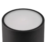 Een close-up van de REALITY Tafellamp FERNANDEZ, een cilindervormige zwarte lamp met een witte ronde bovenkant met een gloeiend krachtsymbool in het midden.