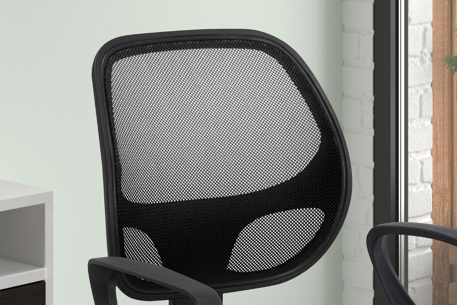 Een close-up van de Bureaustoel 'Hippa' Mesh Zwart (1c), een moderne bureaustoel met een rugleuning van zwart gaas, geplaatst naast een wit bureau bij een raam met een bakstenen muur en groen buiten.