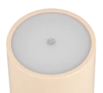 Een close-up van de Reality Tafellamp Fernandez;in, een ronde beige lamp met een platte, lichtgrijze bovenkant en een machtssymbool in het midden.