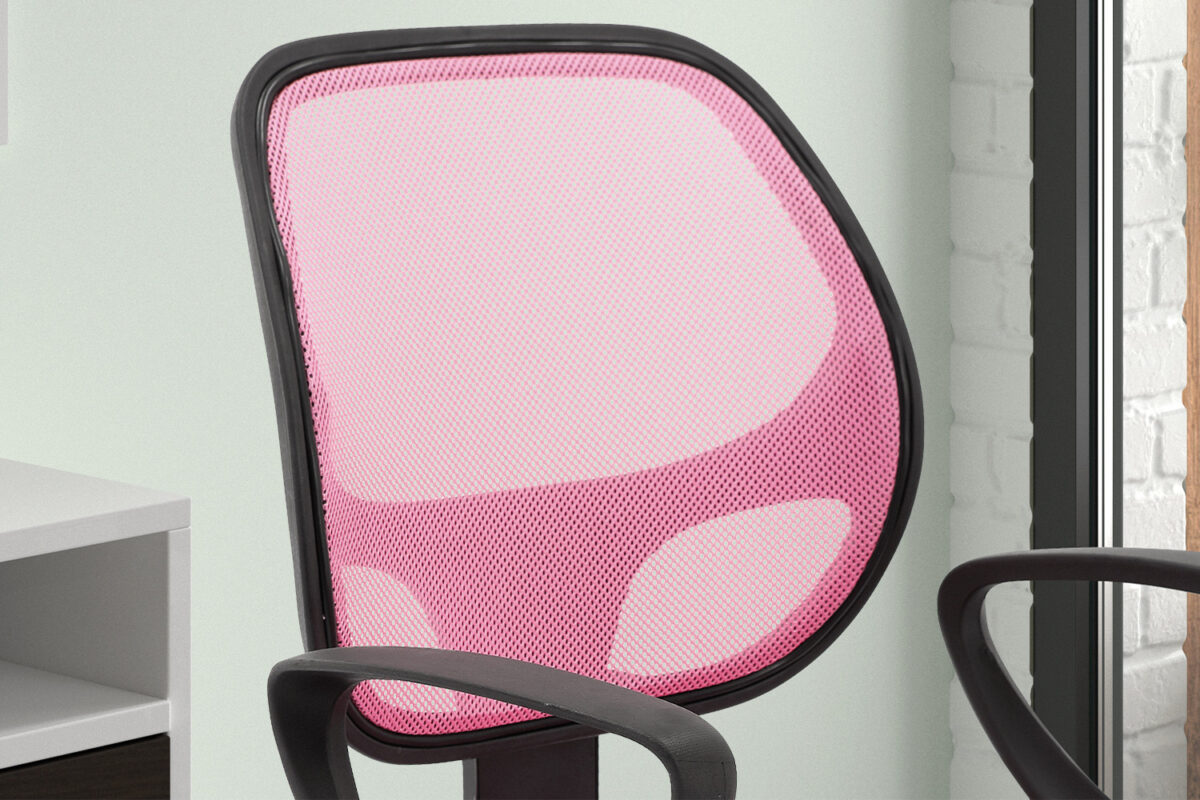 Een close-up van de Bureaustoel 'Hippa' Mesh Roze(1c), met een roze netrugleuning en zwart frame, geplaatst bij een bureau bij een raam met witte bakstenen muren op de achtergrond.