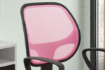 Een close-up van de Bureaustoel 'Hippa' Mesh Roze(1c), met een roze netrugleuning en zwart frame, geplaatst bij een bureau bij een raam met witte bakstenen muren op de achtergrond.