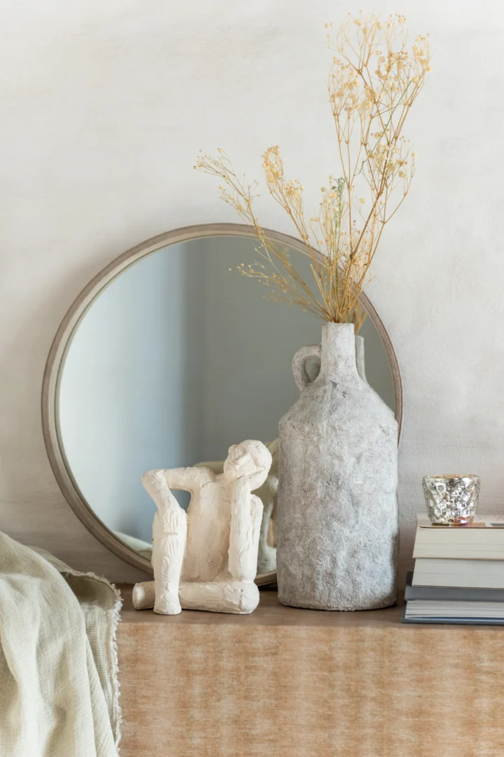 Een kleine ronde beige lederen spiegel staat op een houten oppervlak met een zacht beige doek aan één kant gedrapeerd.