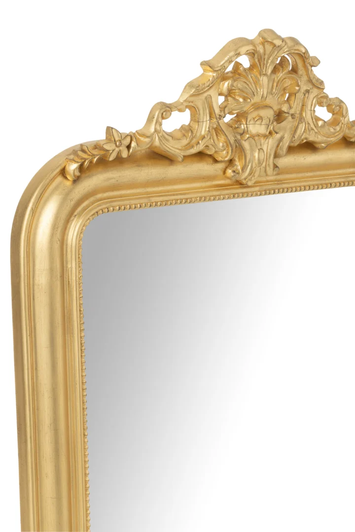 Close-up van de bovenste hoek van de wandspiegel Ema Wood Gold Colored, met ingewikkeld snijwerk van bloemen en bladeren op de sierlijke lijst, waarbij een deel van het reflecterende glas zichtbaar is.