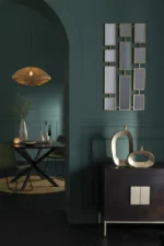 Een moderne eetkamer met donkergroene muren, een ronde tafel en groene stoelen, een geweven hanglamp, metalen vazen op een dressoir van donker hout en de Mirrors 11Parts Metal Gold als geometrisch accent aan de muur.