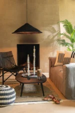 Een gezellige, moderne woonkamer met een Vloerkleed Gevlochten Zeegras-Palmblad Naturel/Zwart vloerkleed, een zwarte stoel, beige bank met gestreepte kussens, ronde zwarte salontafel met kaarsen en decor, geweven mand, potplant en een open haard onder een zwarte hanglamp.