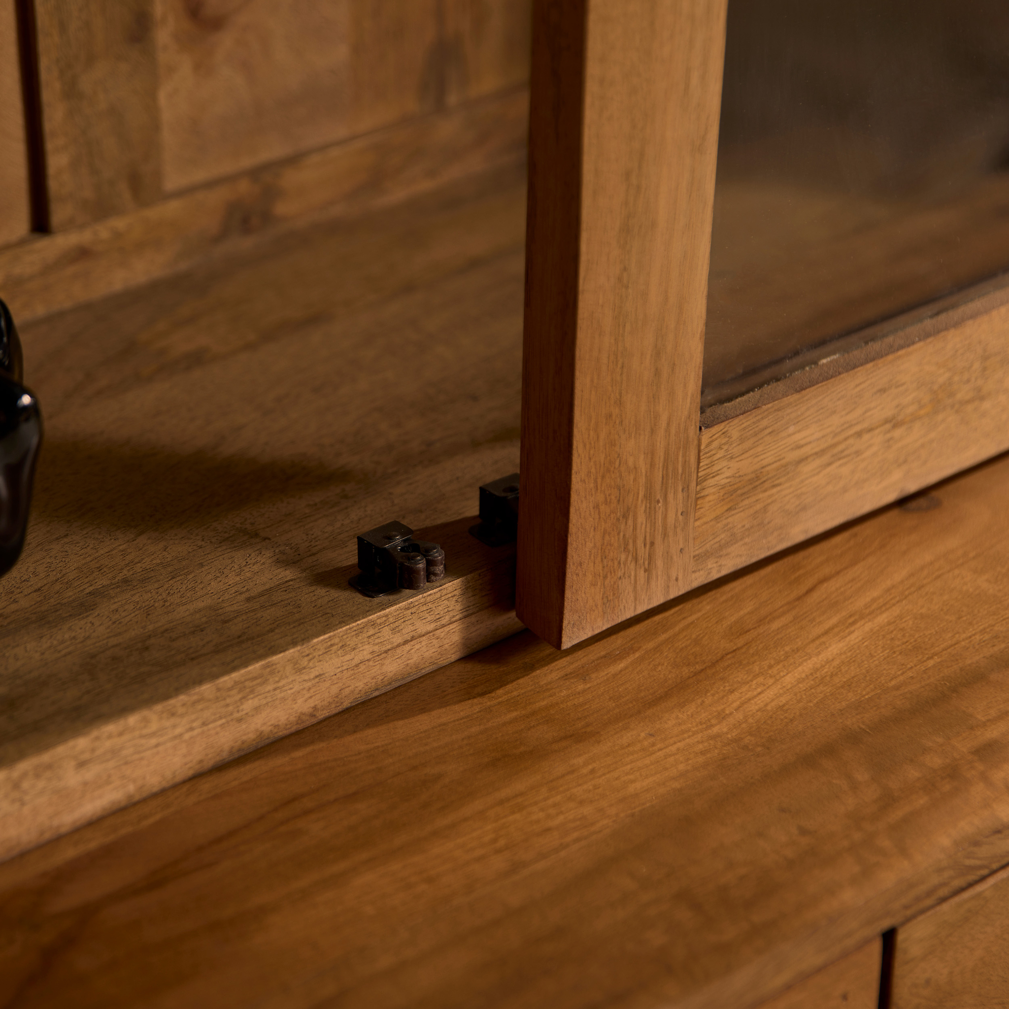 Close-up van de Vitrinekast Boaz XXL, met de nadruk op het metalen grendelmechanisme in de glazen deur en het frame, en met de nadruk op de natuurlijke houtnerf en het vakmanschap.