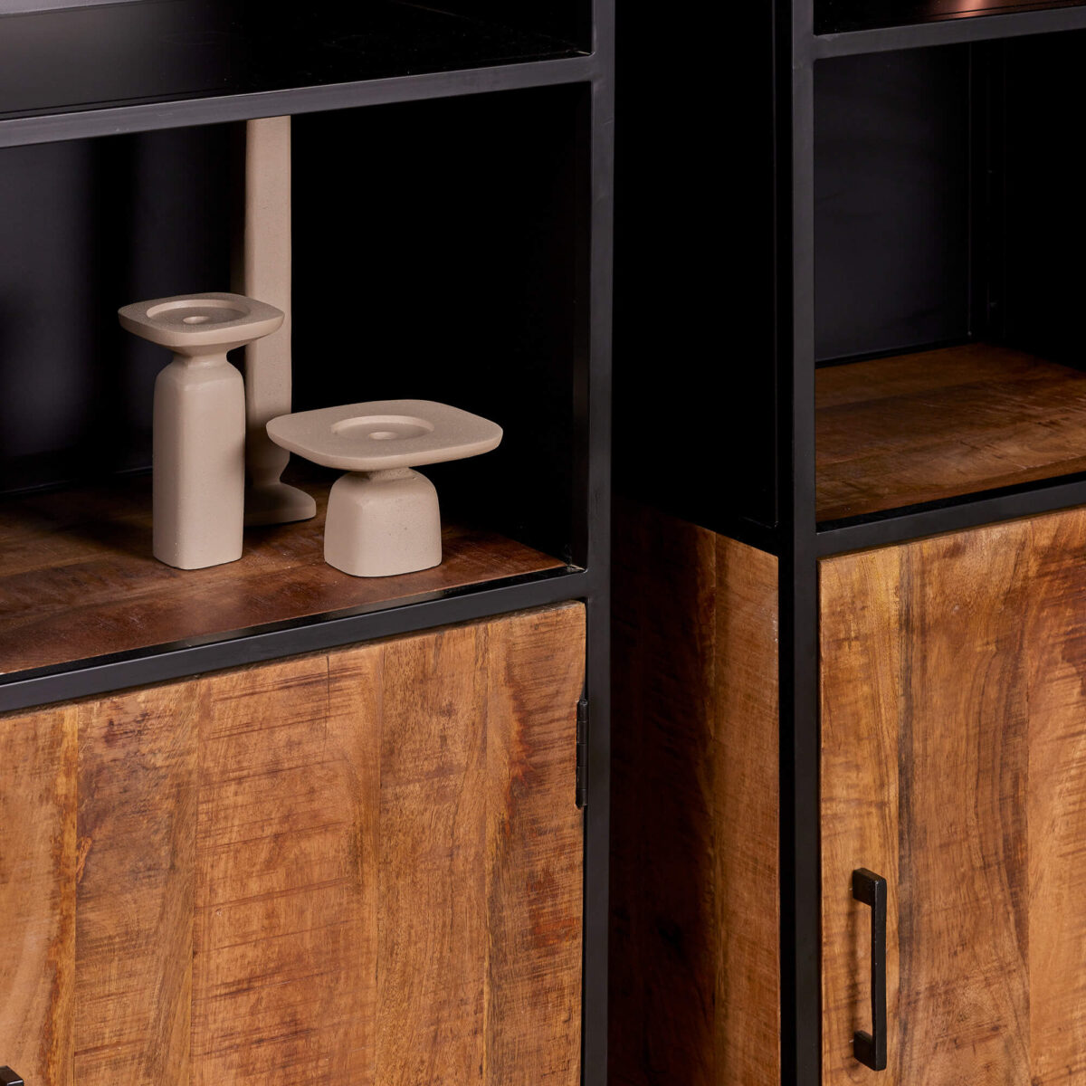 Close-up van de Boekenkast Oakland | 50 cm met houten planken met zwarte metalen frames en twee beige geometrische kaarsenhouders. De onderste kasten hebben een natuurlijke houten afwerking met zwarte handgrepen.